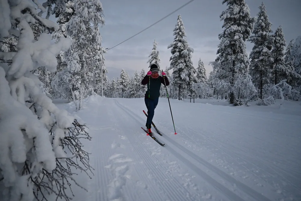 A lone skier on a groomed track through frost-laden forest