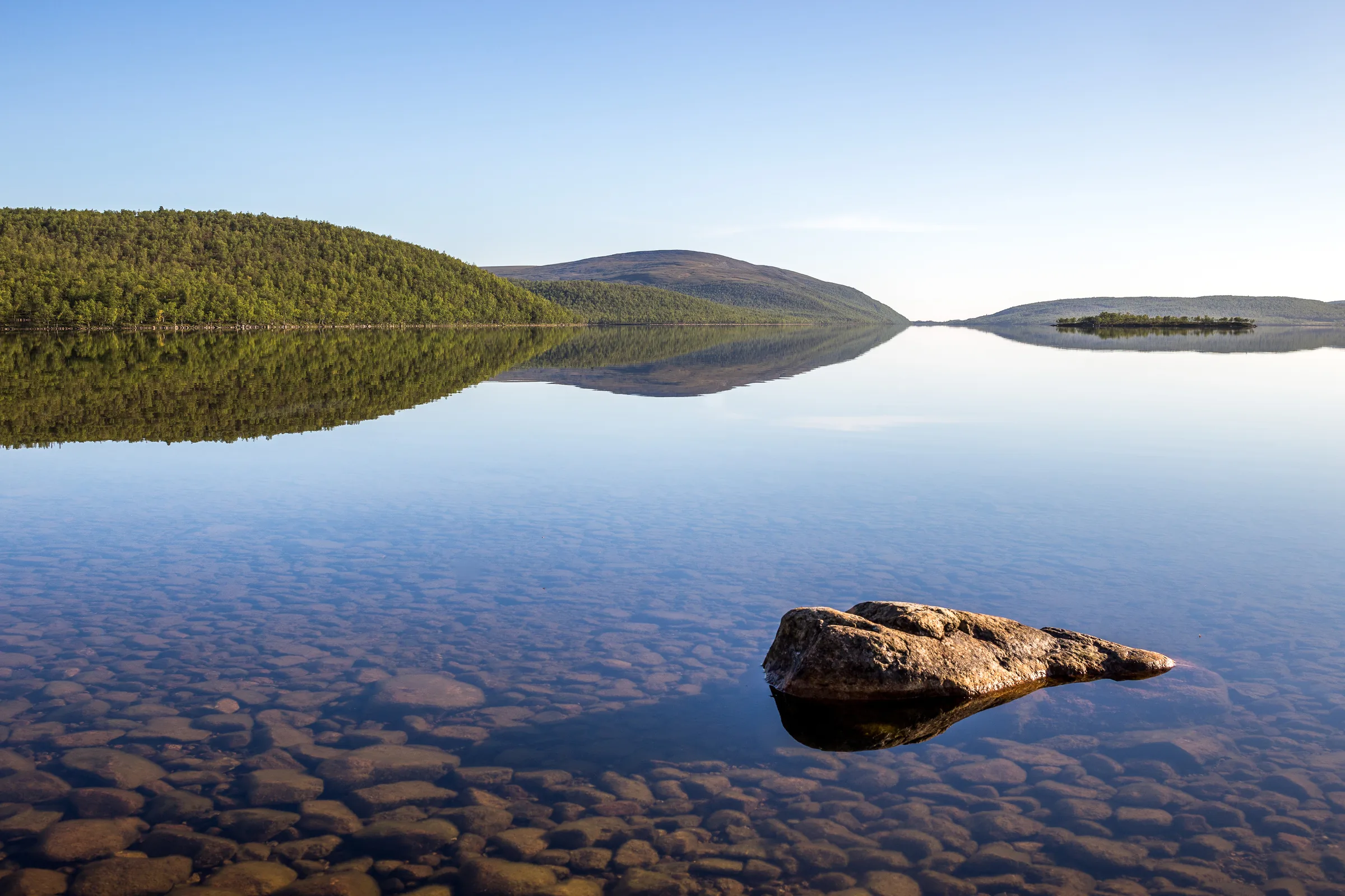 Clear still water reflecting wooded shores and low bare fells